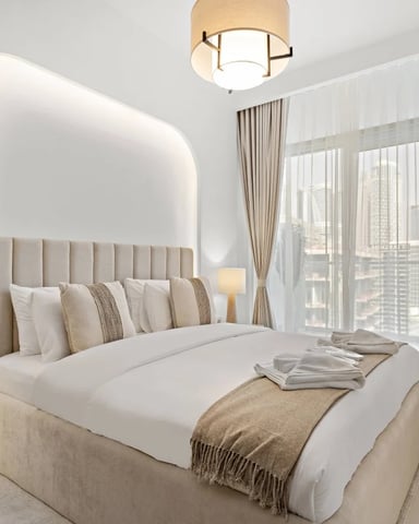 Modern bedroom with upholstered bed, glowing headboard, floor-to-ceiling windows with city views, and neutral furnishings