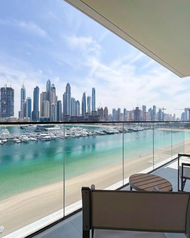 Balcony with lounge chairs overlooking turquoise beach, marina, and high-rise city skyline