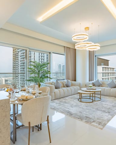 Luxury high-rise apartment with open-plan living and dining area, cream sectional sofa, marble countertops, and floor-to-ceiling windows overlooking city