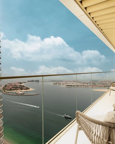 High-rise balcony with woven lounge chairs overlooking waterfront with islands and boats below