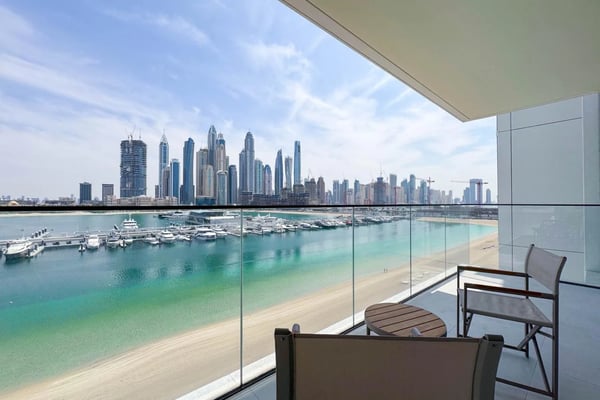 Balcony with lounge chairs overlooking turquoise beach, marina, and high-rise city skyline