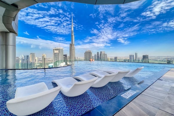Rooftop infinity pool with white loungers overlooking city skyline and tall tower